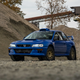 front three-quarter view of a blue Subaru 2.5RS coupe parked among piles of gravel in an industrial setting.
